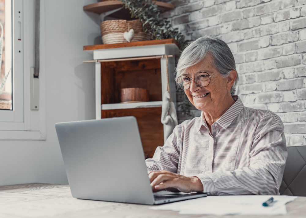 Aged senior female remote worker, happily working from a laptop.