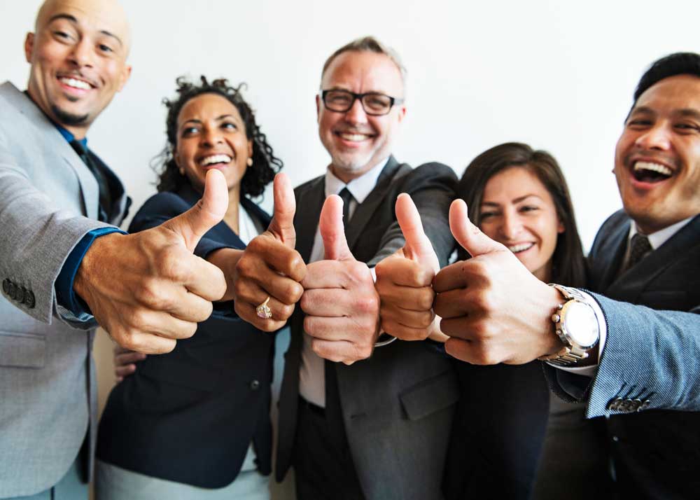 A diverse professional time all shows a "thumbs up" sign while looking enthusiastic and happy.