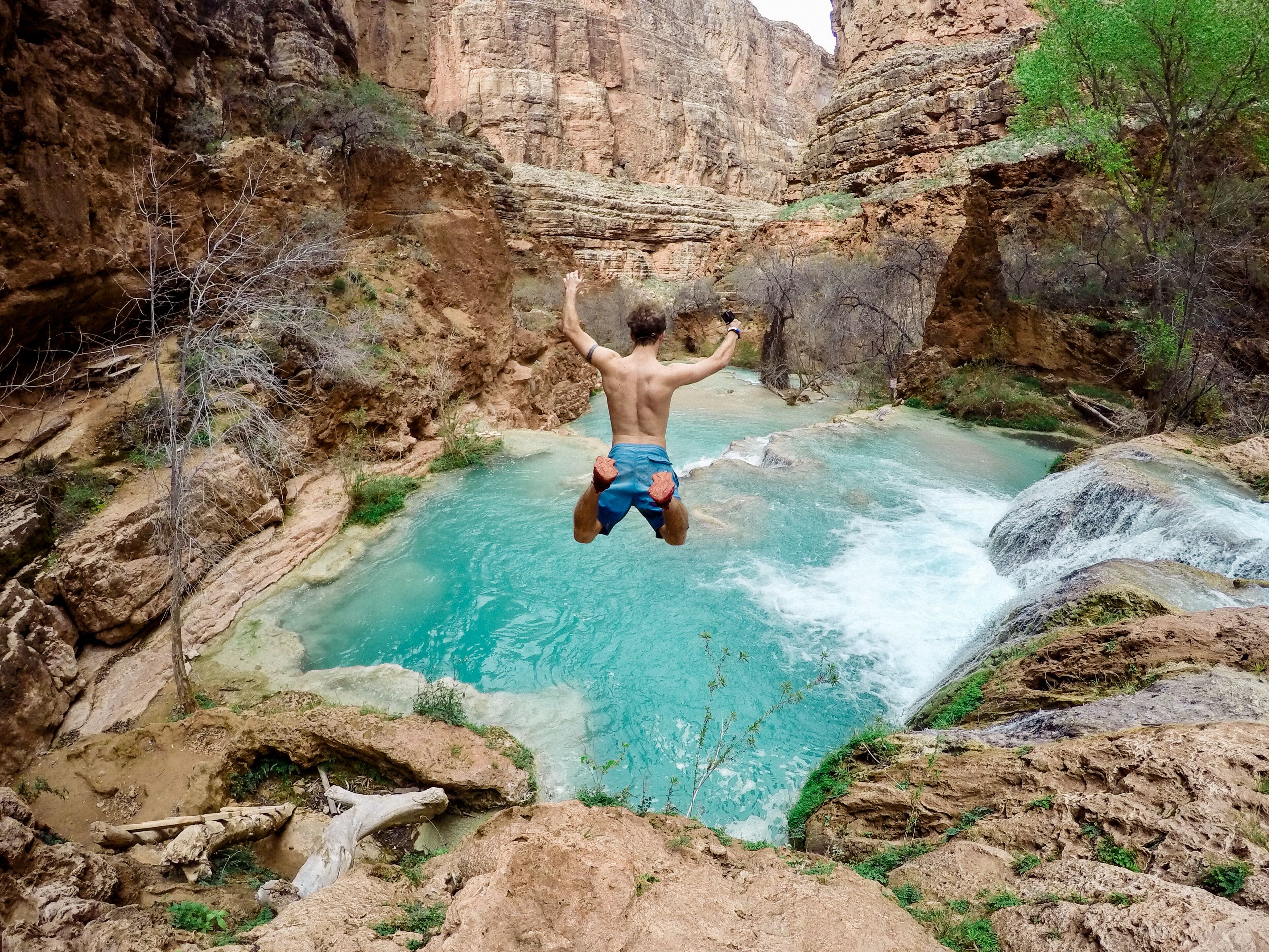 Am image of a young man diving gleefully off the side of a cliff into a mountain pool